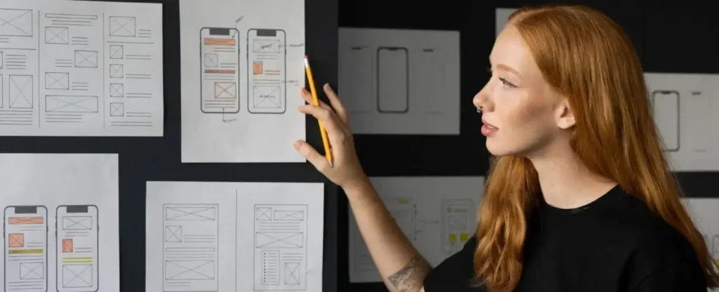 Female UX designer reviewing mobile app wireframes pinned on a wall.